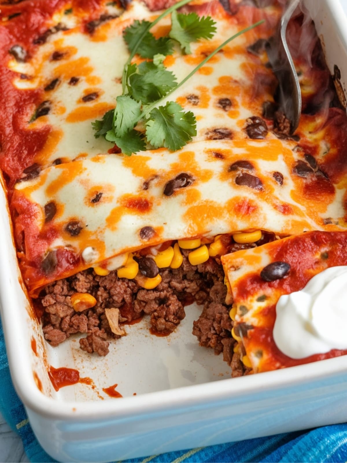 Bubbling beef enchilada bake with golden cheese top, revealing layers of tortillas, seasoned meat, and sauce