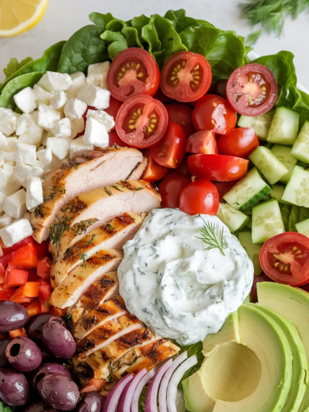 Vibrant Greek chicken bowl with colorful vegetables, olives, feta, and creamy tzatziki on crisp romaine