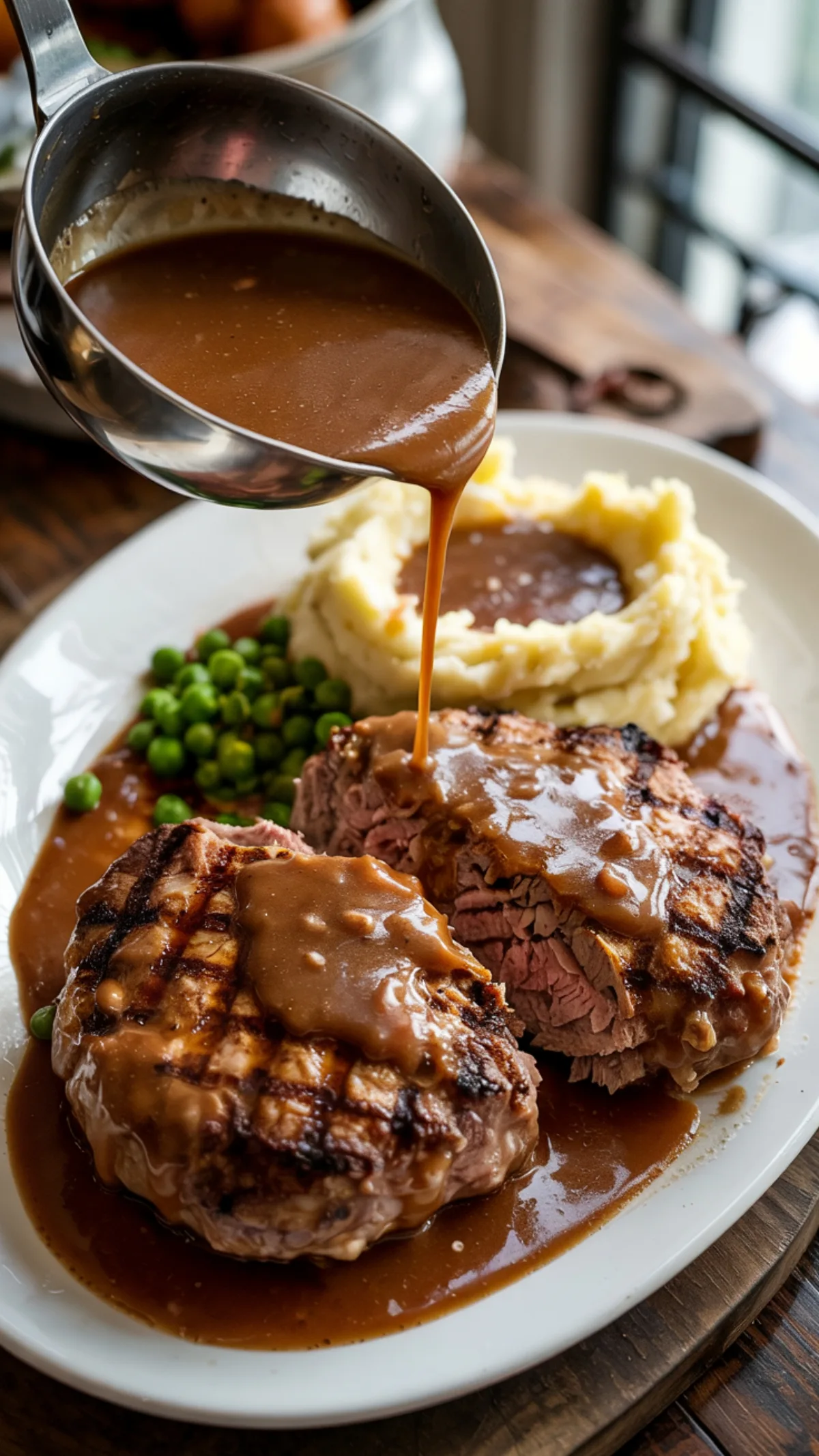 Two juicy Salisbury steaks covered in rich brown gravy with mashed potatoes and peas on white platter